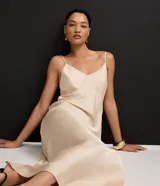 Vestido largo (midi) color beige claro, estilo slip dress, con escote en V y breteles finos ajustables. Presenta un recorte sutil en el área del busto.