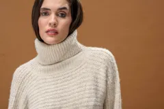 Sweater de punto con cuello alto, manga larga y diseño holgado. Presenta una textura suave con un sutil acabado brillante.
