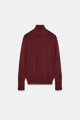 Jersey de punto liso en color beige, con cuello alto y manga larga con detalle de botones metálicos en los puños.