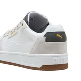 Championes Puma Court Classic de diseño urbano, confeccionados en cuero sintético blanco con refuerzos de gamuza en tono beige. Presentan detalles en azul marino en la lengüeta y el talón, junto con el logo de la marca en dorado. Cuentan con suela de goma color caramelo.