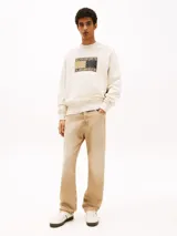 Buzo de algodón color crema, de corte holgado, con cuello redondo, puños y bajo acanalados. Presenta un parche con el logo de Tommy Jeans con estampado de cachemir en el frente y otro parche con el logo en la manga.