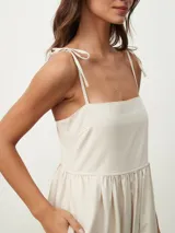 Vestido midi color beige claro, de corte amplio y fluido, con tirantes finos ajustables mediante lazos en los hombros, escote recto y prácticos bolsillos laterales.