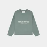 Sweater de tejido de punto color verde agua, con cuello redondo y corte oversize. Presenta un estampado frontal con el texto "EME STUDIOS" y debajo "curated by ben ice".