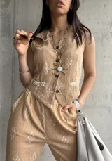 Chaleco beige con estampado de rombos blancos, cuello en V, cierre con botones y bolsillos delanteros ribeteados.