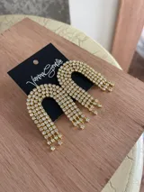 Aros colgantes dorados con forma de arco y múltiples strass incrustados.