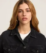 Campera de jeans de corte boxy, color azul medio lavado, con cuello, cierre frontal de botones, bolsillos con solapa y botones en el pecho, y recortes visibles.