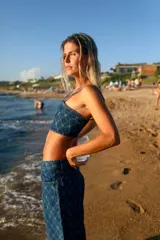 Top corto de denim azul con estampado de monogramas, escote recto, breteles finos y cierre en la espalda.