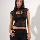 Top de encaje negro con mangas cortas, cuello alto tipo mao y abertura en el pecho con cordones para atar.