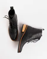 Botas acordonadas estilo borcego, confeccionadas en cuero vacuno negro. Presentan detalles de perforaciones decorativas tipo brogue en la puntera y laterales, con suela y taco de madera en tono natural.