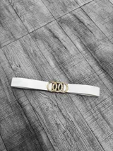 Cinto blanco de cuero sintético con hebilla dorada con forma de eslabones entrelazados.