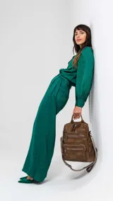 Mochila de símil cuero color marrón con apertura superior y tres bolsillos frontales con cierres metálicos. Cuenta con bolsillos laterales y una correa de galón con diseño geométrico, regulable y extraíble, que permite su uso como bandolera.