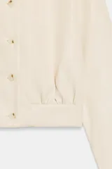 Camisa crop de manga larga con cuello solapa y cierre frontal de botones, confeccionada en tejido sintético con efecto piel color beige.