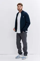 Cardigan de punto color azul marino, con cierre frontal completo, cuello alto y puños acanalados. Presenta un pequeño bordado distintivo en el pecho.