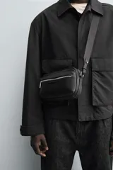 Bandolera negra con textura grabada, compartimento principal con cierre de cremallera, bolsillo interior con cremallera, bolsillo frontal con cremallera y asa de hombro ajustable.