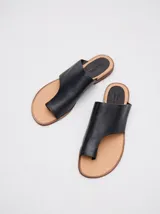 Sandalias chatas de cuero negro, con diseño geométrico y minimalista que incluye tira ancha y sujeción para el dedo.