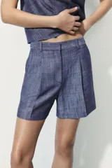 Bermuda de tiro alto con diseño de pliegues en el frente. Cuenta con cintura con trabillas, bolsillos laterales ocultos en las costuras y cierre frontal con cremallera, botón y ganchos metálicos.
