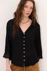 Camisa de lino color blanco, con escote en V, mangas tres cuartos con detalles de encaje en los puños y ruedo asimétrico más largo en la parte trasera.