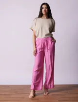 Pantalón ancho de lino y rayón color fucsia, con cintura elastizada y cordón de ajuste. Presenta bolsillos delanteros y ruedo con tajo y flecos.