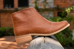 Botín de cuero con textura grabada tipo reptil, color marrón. Presenta un diseño de caña baja con cierre frontal y taco cuadrado bajo con acabado de suela.