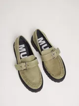 Mocasines de cuero color verde oliva con detalle de hebilla metálica ajustable en el empeine. Presentan costuras reforzadas en la puntera y suela de goma negra con plataforma dentada.