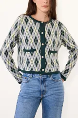 Saco de punto con diseño de rombos en tonos verde, amarillo y gris. Presenta cuello redondo, cierre frontal con botones y dos bolsillos delanteros con terminaciones en contraste.