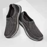 Mocasín Skechers Relaxed Fit Expected Avillo, color gris denim, de lona tejida con efecto deslavado y capas superpuestas de ante. Cuenta con plantilla Skechers Memory Foam, paneles elásticos laterales y suela de goma.