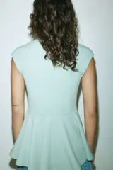 Top entallado de punto roma color verde menta, con diseño sin mangas de hombros cubiertos, cuello alto y corte peplum con vuelo en la parte inferior.