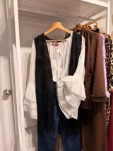 Blusa romántica de color blanco, confeccionada en tejido ligero y semitransparente, con escote redondo fruncido y cordones ajustables con tiras colgantes. Presenta mangas largas amplias de diseño fluido.