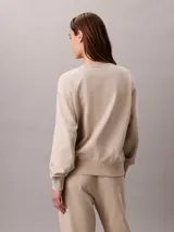 Buzo de felpa Calvin Klein de color beige, con cuello redondo, manga larga y detalles de canalé en cuello, puños y bajo. Presenta un emblema con logo texturizado en el pecho.