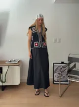 Chaleco sin mangas, confeccionado con cuadrados de cuero negro perforado combinados con cuadrados de crochet en hilo de algodón negro y blanco, con detalles centrales en rojo.