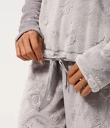 Conjunto de pijama largo de dos piezas confeccionado en tejido fleece suave y abrigado. Incluye una blusa de manga larga con cuello redondo y ajuste en la cintura, y un pantalón con cintura elástica. Ambas prendas presentan una textura grabada con diseño de gatitos.