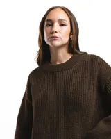 Buzo unisex de tejido de punto grueso en lana merino, color rojo, con cuello redondo y diseño de calce relajado. Presenta un detalle bordado a mano en contraste en la manga.