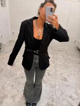 Blazer de largo medio con diseño a cuadros en tonos tierra, confeccionado en mezcla de algodón y poliéster. Presenta solapas clásicas, bolsillos laterales y un cinto de cuero fino incorporado para ajustar la cintura.