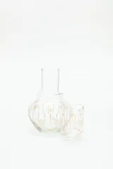 Jarra de vidrio transparente con diseño de estrellas doradas. Incluye un vaso de vidrio transparente con diseño de líneas verticales doradas.