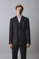 Blazer de corte regular fit confeccionado en lana italiana, con diseño de raya diplomática. Presenta cuello con solapas de pico, cierre frontal de botonadura cruzada, bolsillos de vivo en el pecho y bolsillos de solapa en la cadera.