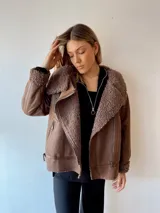 Campera marrón de gamuza sintética con interior de piel sintética color beige. Tiene cuello solapa con hebilla, cierre cruzado con cremallera y bolsillos laterales con cremallera.