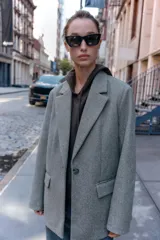 Blazer de corte recto y diseño minimalista, confeccionado en tejido de paño suave color beige. Presenta cuello con solapas clásicas, cierre frontal con un solo botón y dos bolsillos delanteros con solapa.