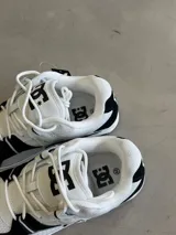 Championes DC Manteca 4, color blanco con detalles en negro. Presentan una parte superior de malla y cuero sintético, con el logo de DC en la lengüeta y el lateral. Cuentan con cordones blancos y una suela de goma.