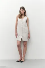 Vestido corto color beige melange, de corte sastrero y confeccionado en lino. Presenta escote en V, cierre frontal con botones y un bolsillo de parche en el pecho.