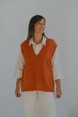 Chaleco de punto color terracota con escote en V profundo y detalle de trenzas verticales en el frente. Presenta un diseño holgado con aberturas laterales y terminaciones en rib acanalado.