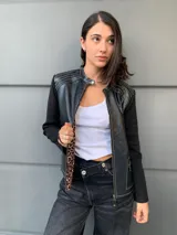 Campera negra con cuerpo de cuero sintético y mangas largas de tejido de punto fino. Presenta cierre frontal con cremallera, cuello redondo y bolsillos con cierre en el frente. Detalles de costuras en color blanco.