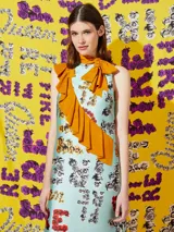 Vestido midi celeste con estampado de flores y texto, con volado amarillo en diagonal y lazo en el cuello.