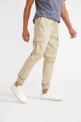 Pantalón cargo color beige con ajuste slim, cintura elástica con cordón ajustable, bolsillos laterales con solapa y velcro, y puños elásticos en los tobillos.