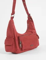 Cartera de hombro color rojo, confeccionada en símil gamuza, con diseño de múltiples bolsillos externos, incluyendo uno frontal con cierre y dos laterales. Cuenta con correa ajustable y logo metálico de la marca en el frente.
