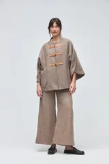 Capa de lana fina sin teñir, con diseño de corte amplio y mangas tipo kimono. Presenta cierre frontal mediante tres alamares de cuero.