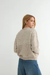 Campera tejida de punto con diseño a rayas horizontales en tonos beige y gris. Presenta cierre frontal completo, cuello redondo, bolsillos delanteros y puños y ruedo acanalados.