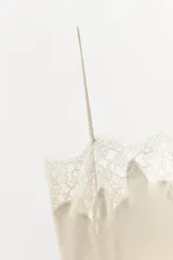 Vestido midi de estilo lencero confeccionado en tejido satinado color beige. Presenta escote recto con tirantes finos y aplicaciones de encaje a tono en el escote y en el ruedo.