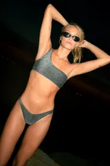 Bikini de tela lúrex color plateado con acabado brillante. El corpiño es tipo top a un hombro con hebilla decorativa y ribetes en color negro. La bombacha es de corte vedetina.