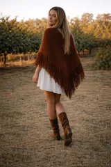 Ruana tejida de lana merino en color marrón, con diseño de flecos en todo el borde inferior. Presenta una textura suave y cálida, ideal para superponer sobre otras prendas.