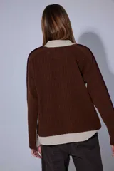 Saco de punto acanalado en color gris claro, con cierre frontal de botones oscuros. Presenta un diseño de bloques de color en las mangas, combinando negro y marrón, y un cuello redondo.